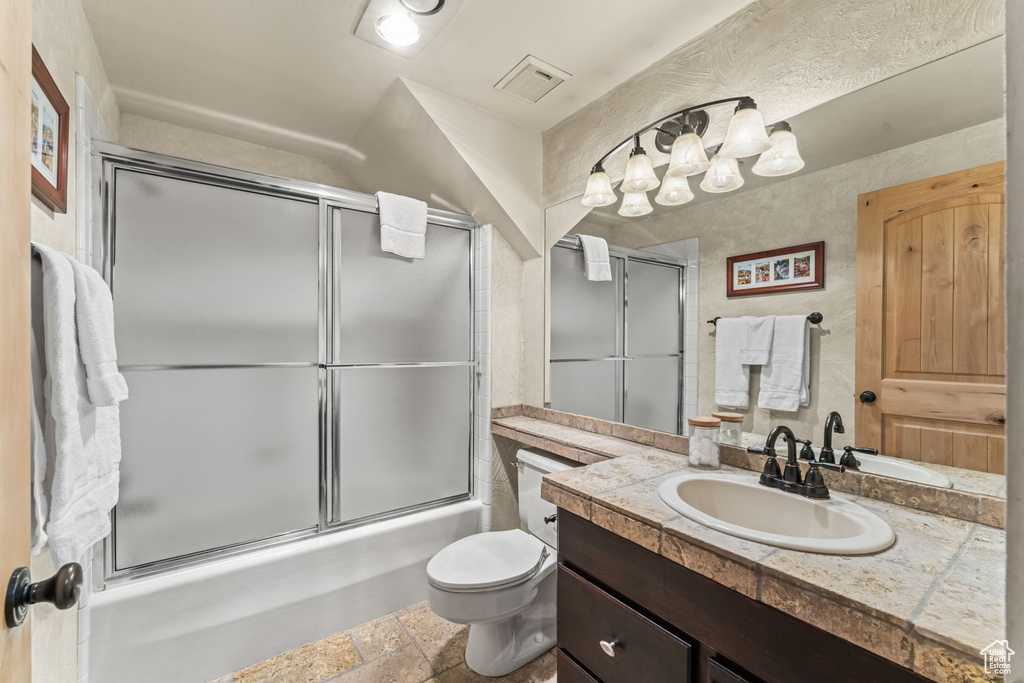 Full bathroom with large vanity, toilet, tile floors, and bath / shower combo with glass door