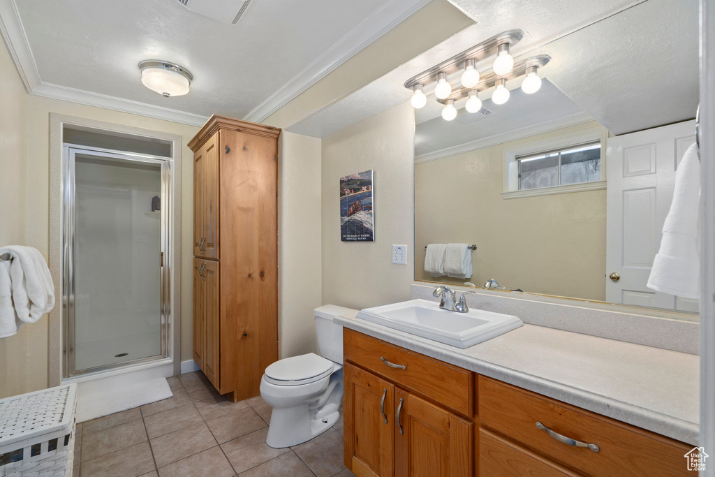 Bathroom with large vanity, ornamental molding, toilet, a shower with shower door, and tile flooring