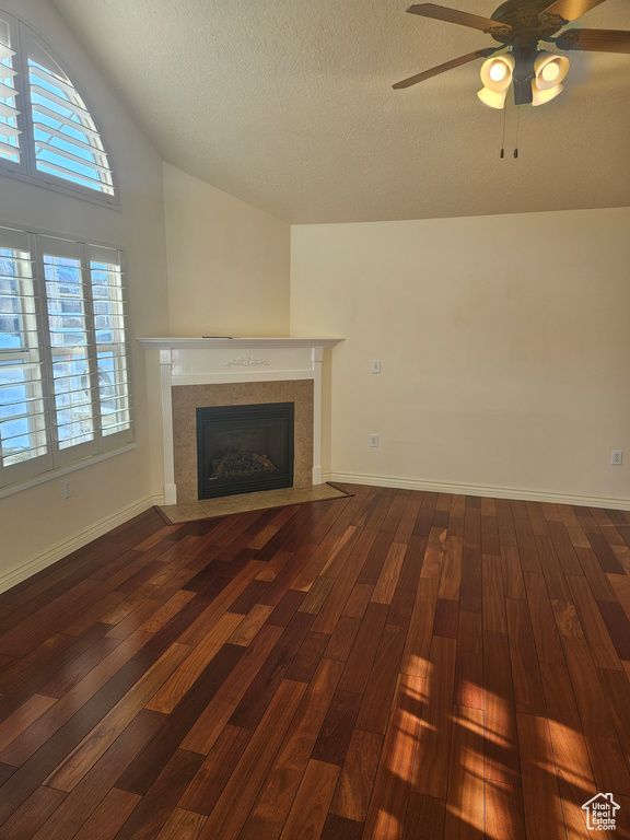 Unfurnished living room featuring dark hardwood / wood-style floors, vaulted ceiling, ceiling fan, and a textured ceiling