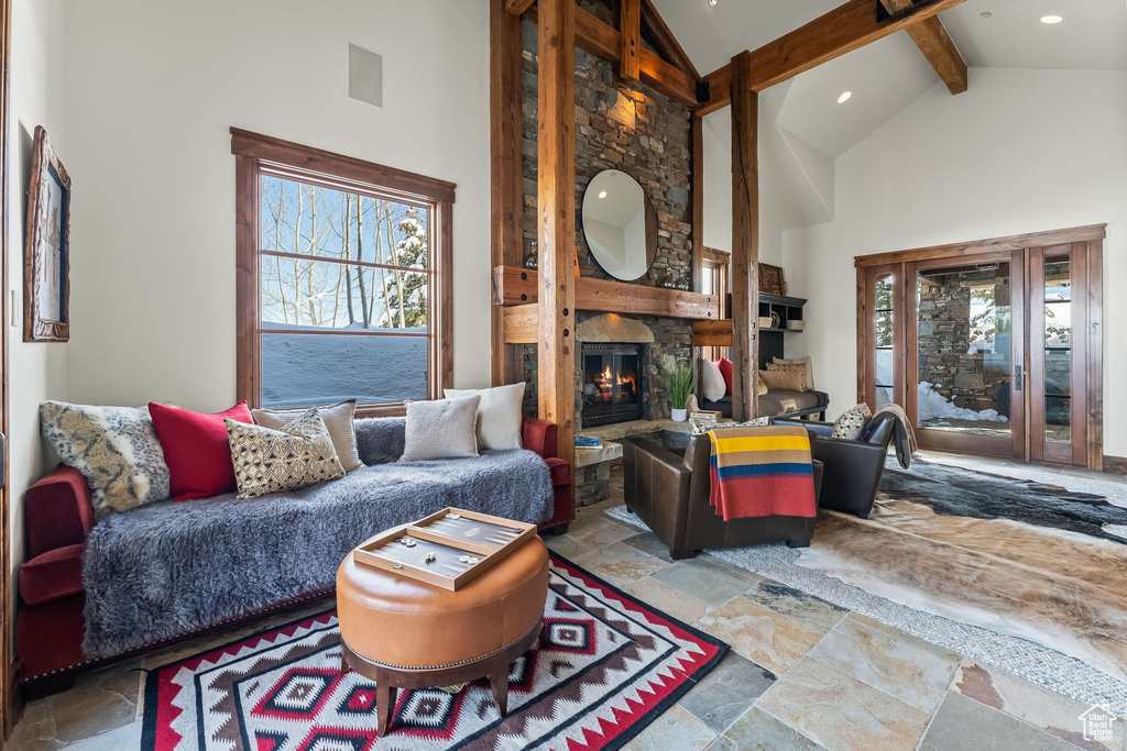 Living room featuring high vaulted ceiling, beam ceiling, tile floors, and a stone fireplace