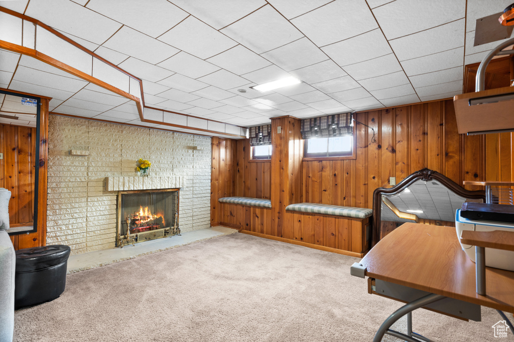 Office space featuring wood walls, light colored carpet, a paneled ceiling, and a brick fireplace