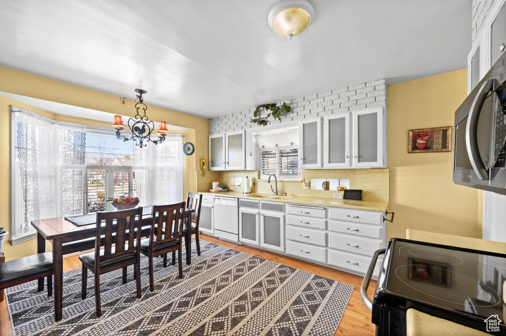 Kitchen with dishwasher, range, an inviting chandelier, light hardwood / wood-style flooring, and decorative light fixtures