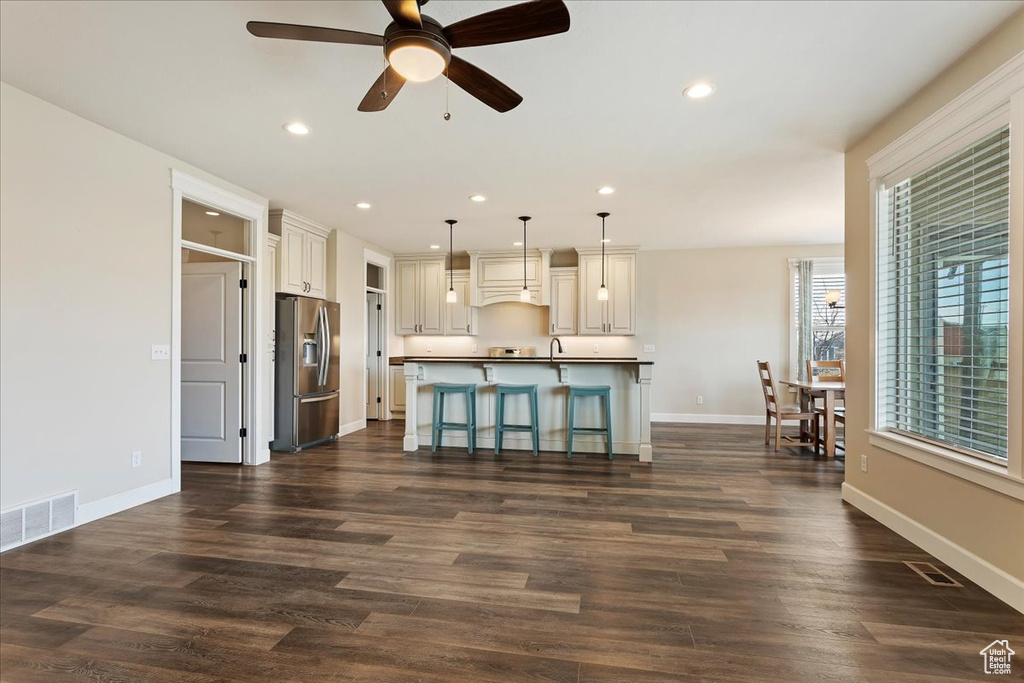 Interior space featuring a kitchen island with sink, dark hardwood / wood-style flooring, a kitchen bar, stainless steel refrigerator with ice dispenser, and ceiling fan