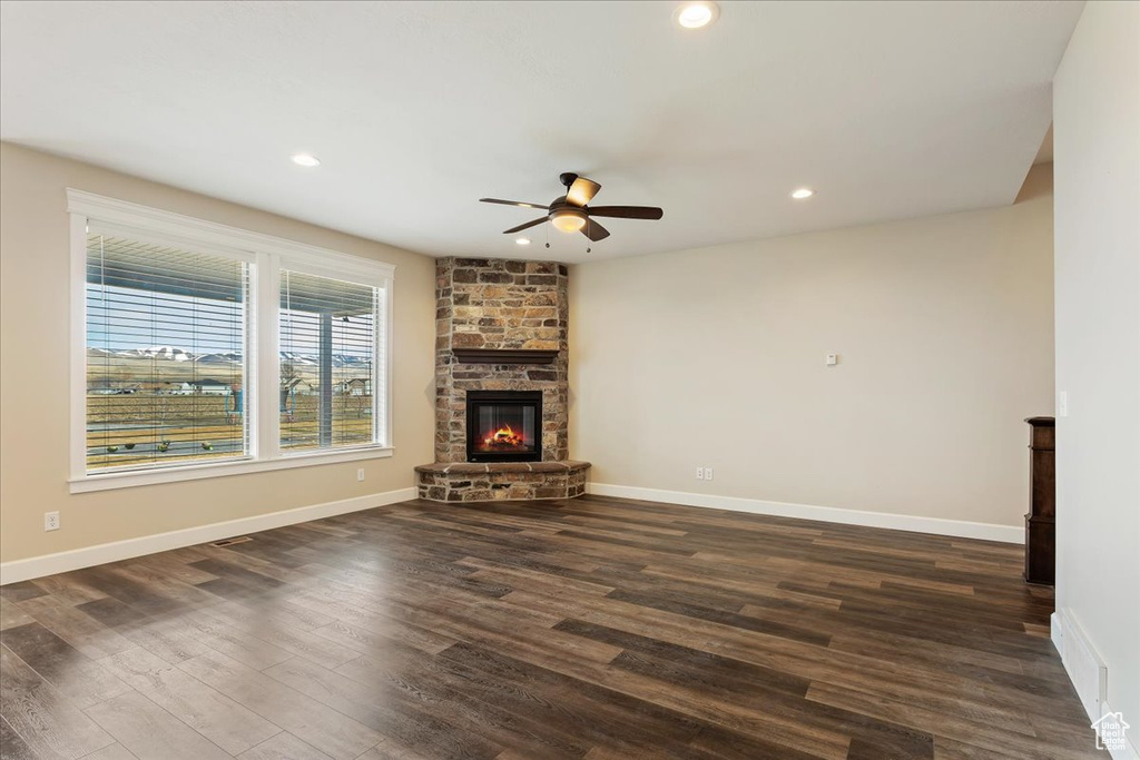 Unfurnished living room with a fireplace, dark wood-type flooring, and ceiling fan