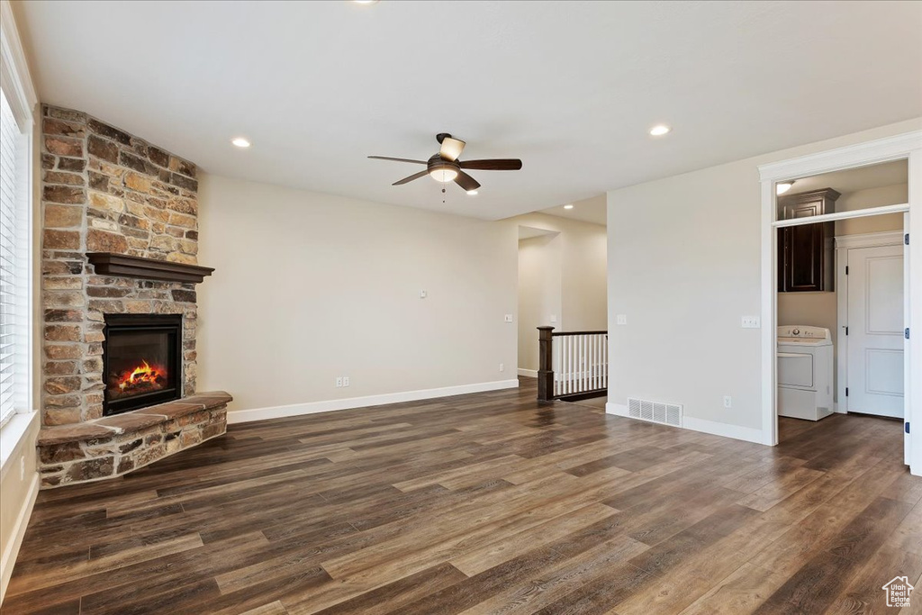 Unfurnished living room featuring washer / dryer, dark hardwood / wood-style flooring, ceiling fan, and a stone fireplace