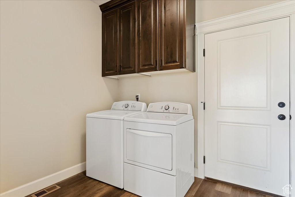 Clothes washing area featuring dark wood-type flooring, cabinets, and washing machine and dryer