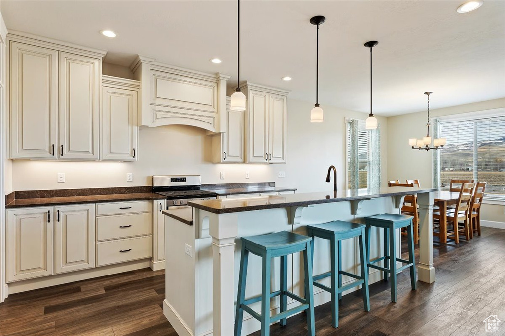 Kitchen with custom range hood, dark wood-type flooring, an inviting chandelier, pendant lighting, and an island with sink
