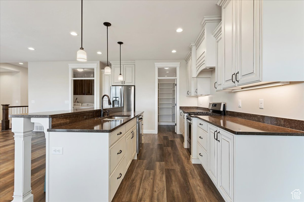 Kitchen with dark hardwood / wood-style floors, a kitchen island with sink, appliances with stainless steel finishes, a kitchen breakfast bar, and hanging light fixtures