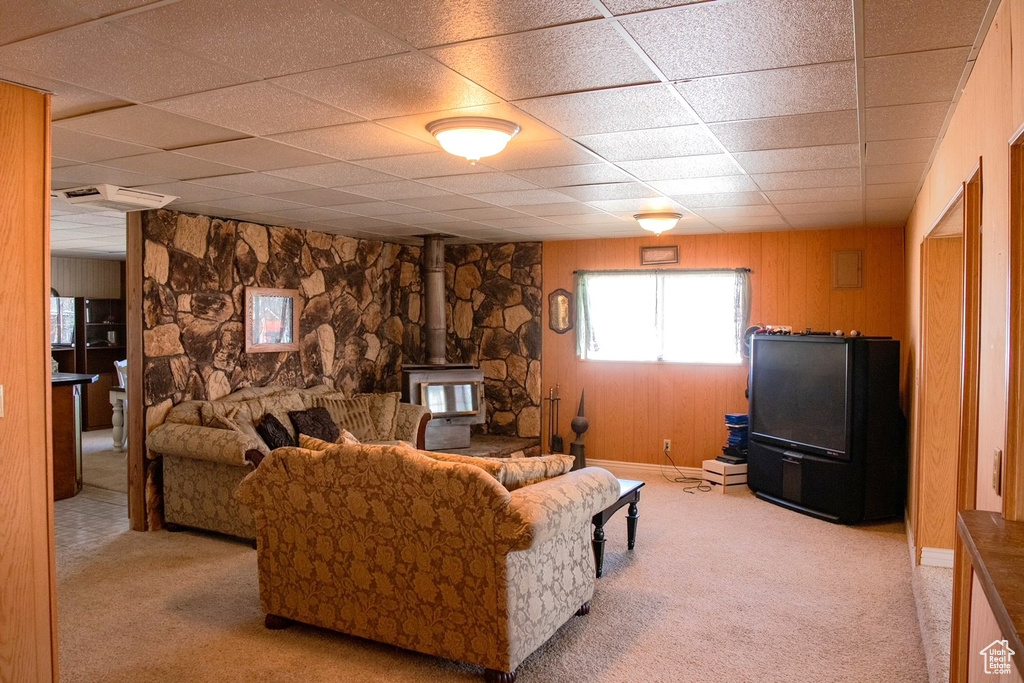 Carpeted living room with wood walls, a wood stove, and a paneled ceiling