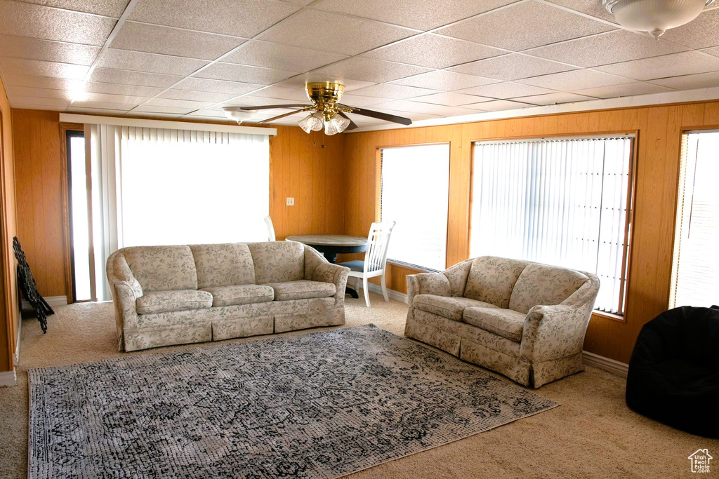 Carpeted living room featuring ceiling fan, wooden walls, and a paneled ceiling