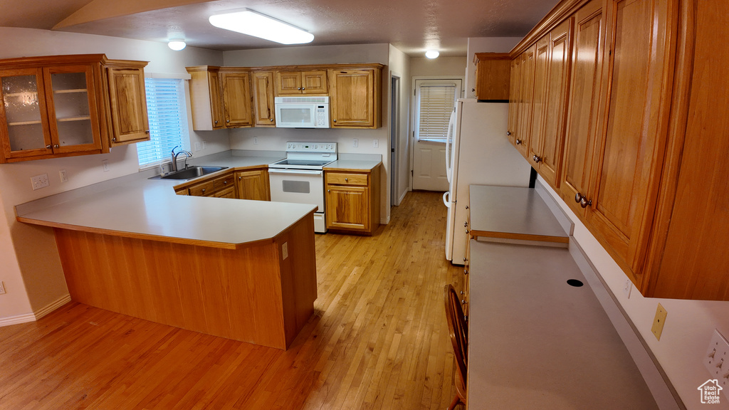 Kitchen with white appliances, light hardwood / wood-style flooring, kitchen peninsula, and sink