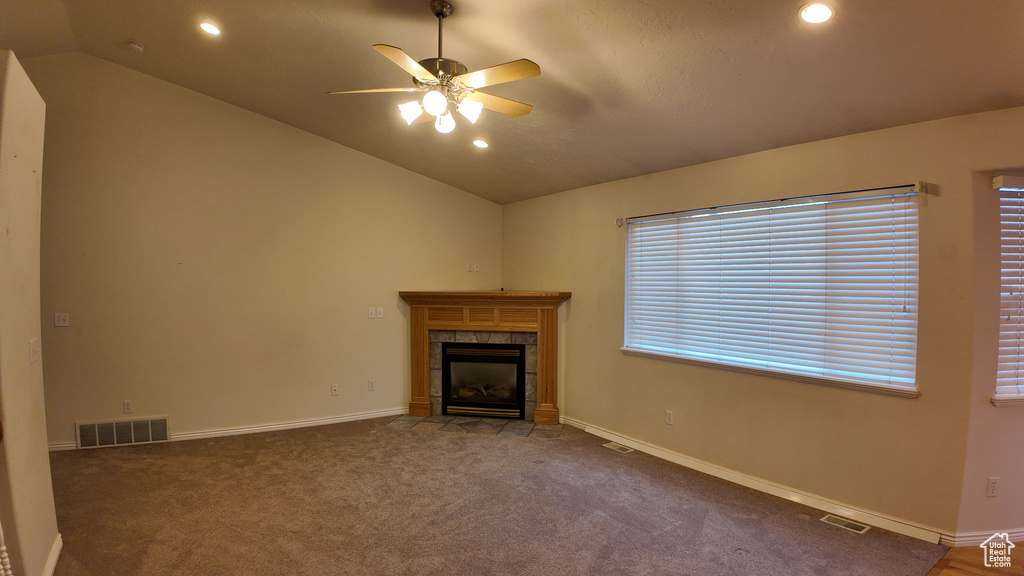 Unfurnished living room with a tiled fireplace, dark colored carpet, ceiling fan, and lofted ceiling