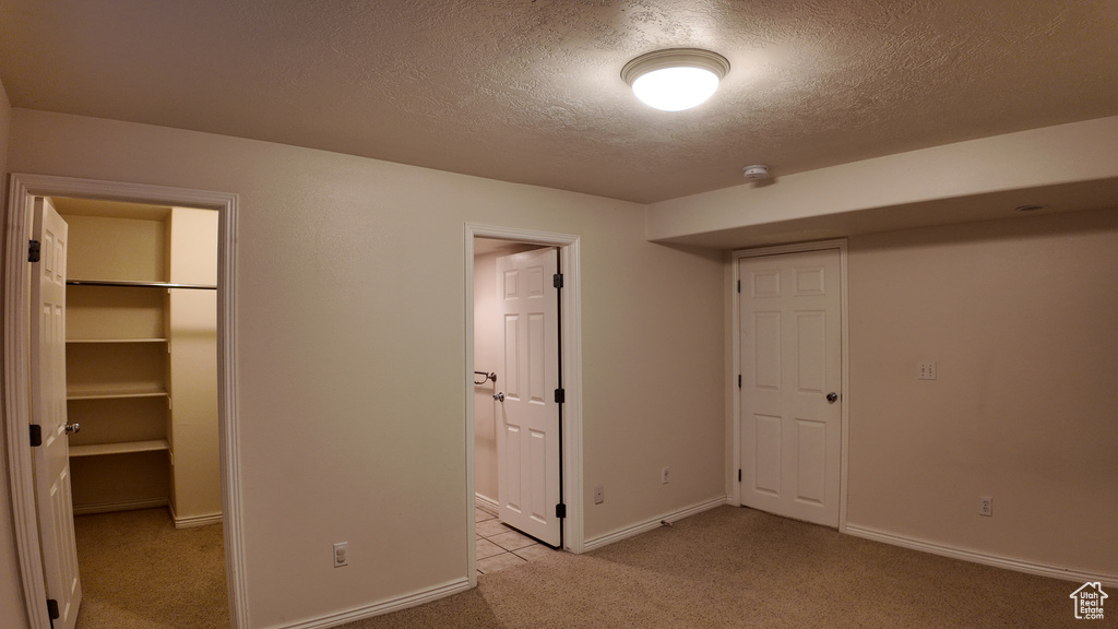 Unfurnished bedroom featuring a walk in closet, a closet, light carpet, and a textured ceiling