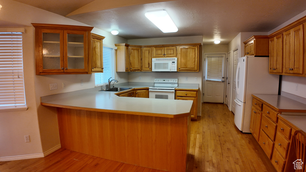 Kitchen featuring white appliances, light hardwood / wood-style floors, kitchen peninsula, and sink