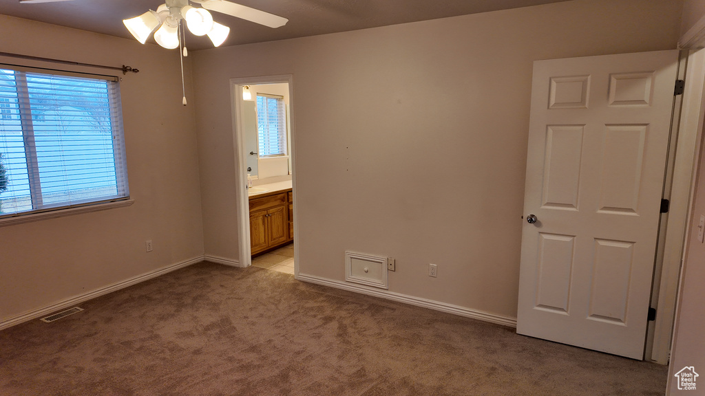 Unfurnished bedroom with ensuite bathroom, ceiling fan, and light carpet