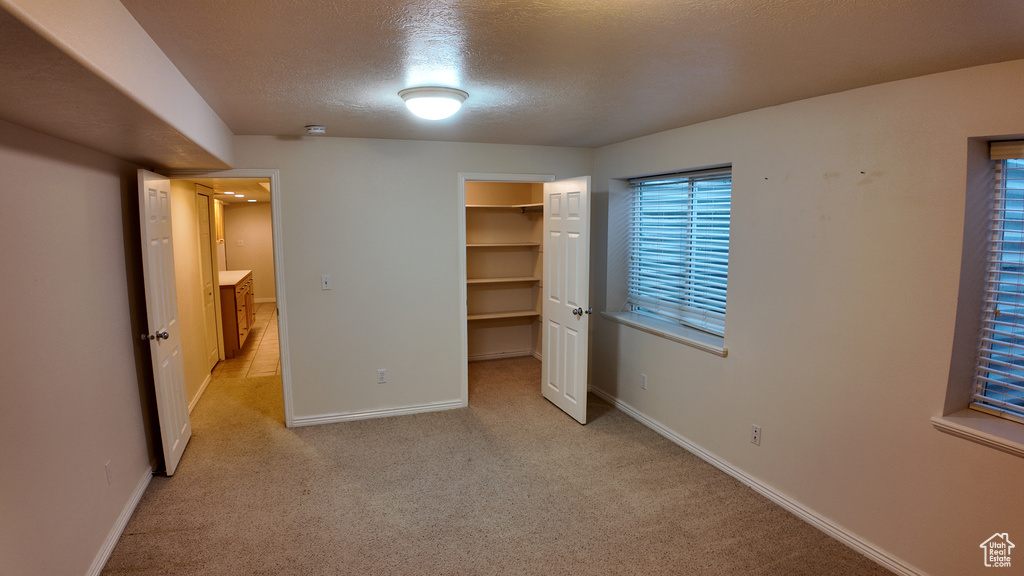 Unfurnished bedroom featuring a walk in closet, a closet, light colored carpet, and a textured ceiling
