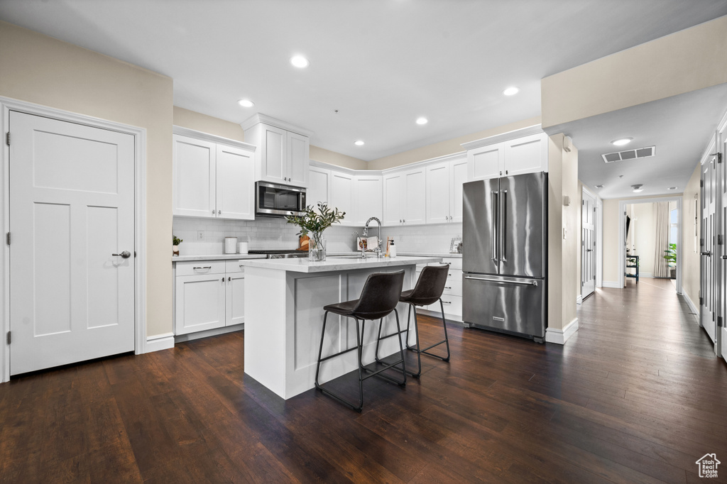Kitchen with dark hardwood / wood-style floors, appliances with stainless steel finishes, a breakfast bar, and white cabinetry