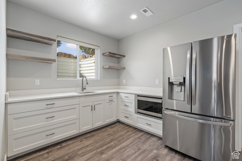 Kitchen with stainless steel appliances, white cabinetry, sink, and dark wood-type flooring