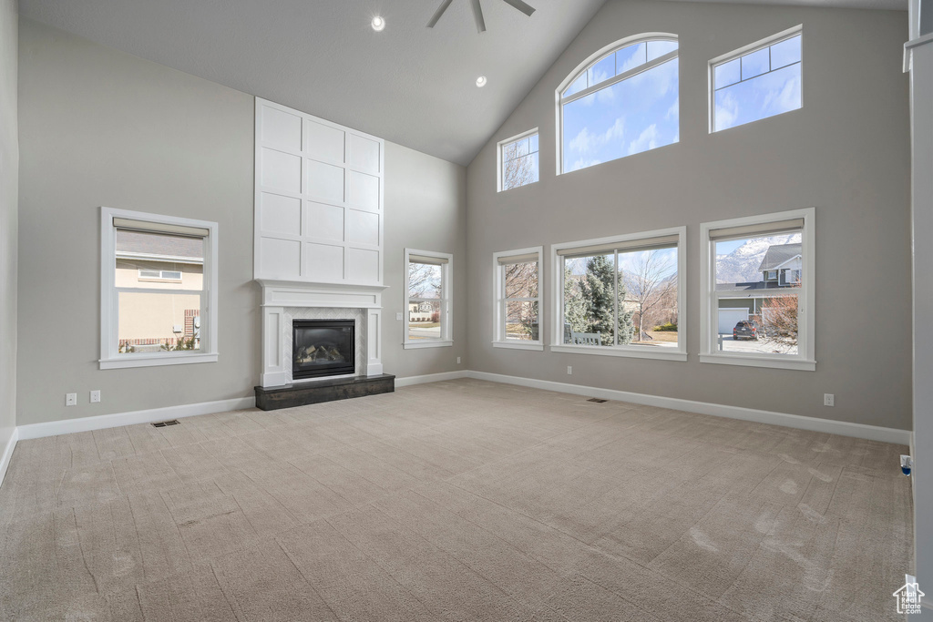 Unfurnished living room featuring a fireplace, high vaulted ceiling, light carpet, and ceiling fan