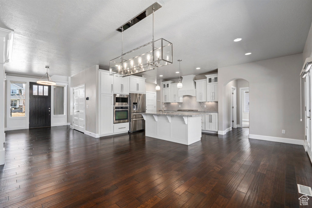 Kitchen featuring premium range hood, dark hardwood / wood-style flooring, white cabinetry, a breakfast bar, and hanging light fixtures