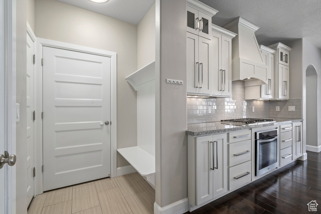 Kitchen featuring dark hardwood / wood-style floors, stainless steel appliances, white cabinets, custom range hood, and backsplash