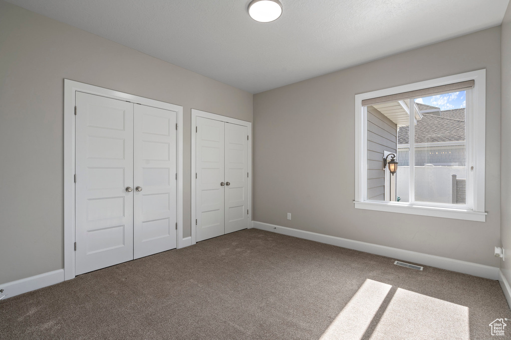 Unfurnished bedroom featuring dark carpet and two closets