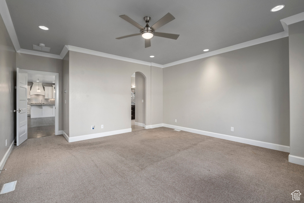 Unfurnished bedroom featuring ceiling fan, ornamental molding, and light carpet