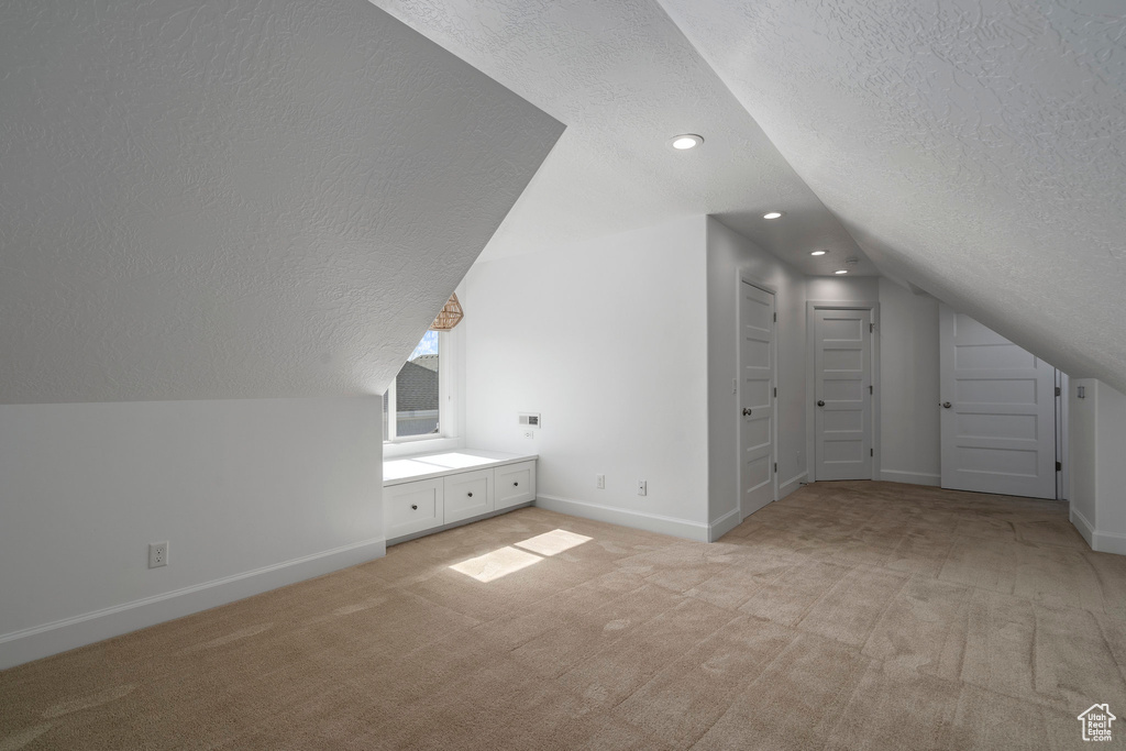 Bonus room with lofted ceiling, light carpet, and a textured ceiling