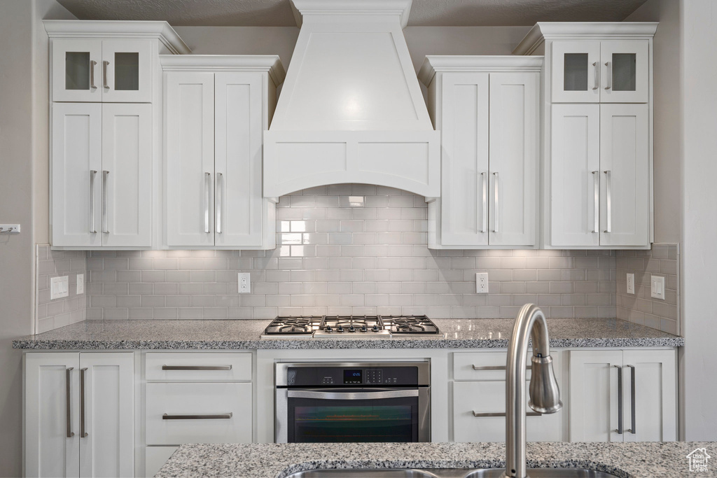 Kitchen featuring tasteful backsplash, appliances with stainless steel finishes, custom exhaust hood, and white cabinets