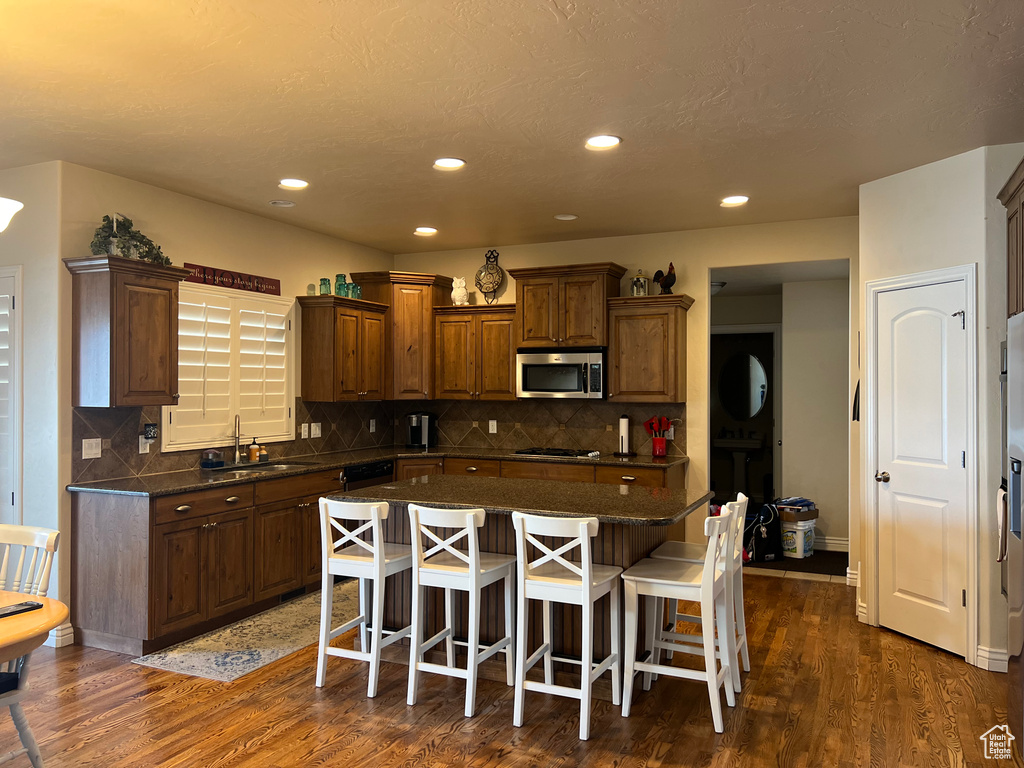 Kitchen with dark hardwood / wood-style floors, stainless steel appliances, a kitchen breakfast bar, and tasteful backsplash