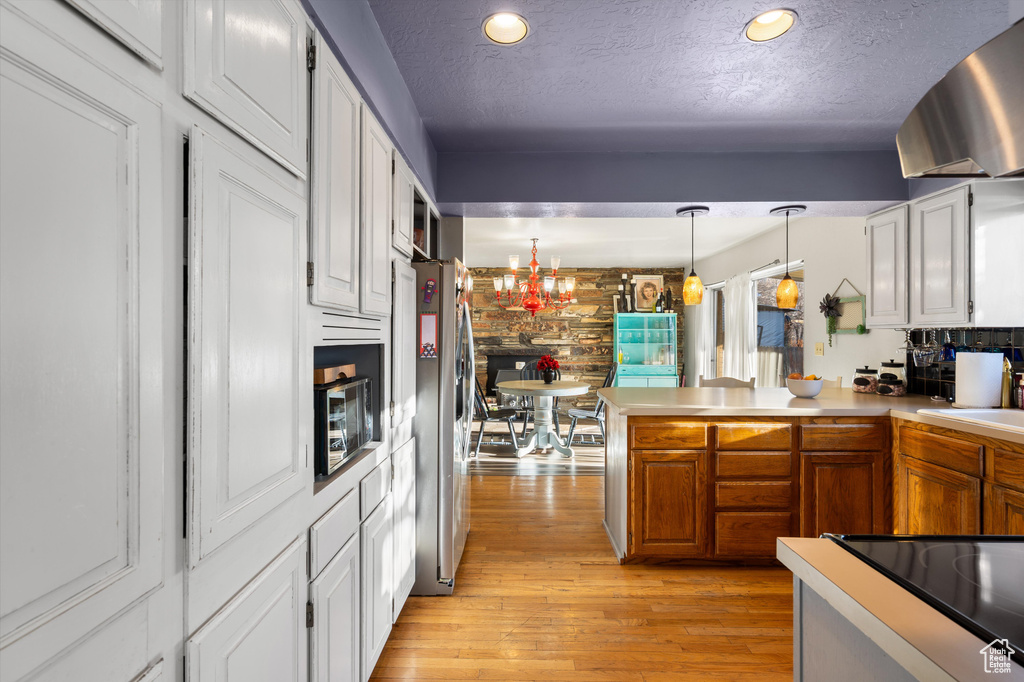 Kitchen featuring pendant lighting, light hardwood / wood-style flooring, kitchen peninsula, stainless steel refrigerator, and a notable chandelier