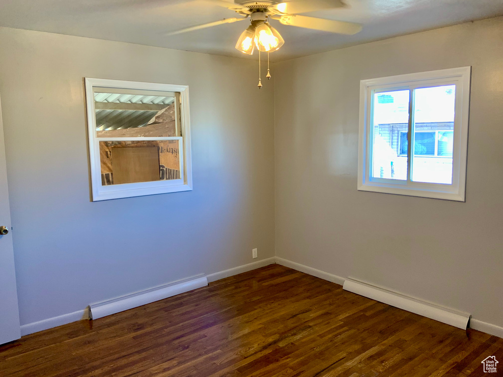 Empty room featuring a baseboard heating unit, ceiling fan, and dark wood-type flooring