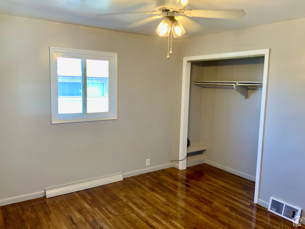 Unfurnished bedroom featuring a closet, dark hardwood / wood-style flooring, a baseboard heating unit, and ceiling fan