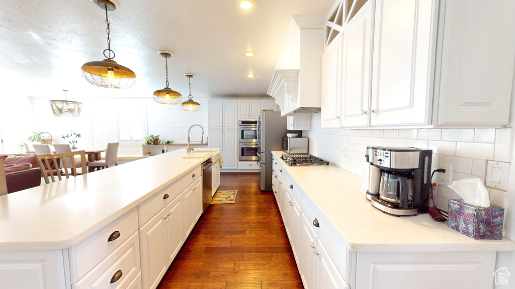 Kitchen featuring dark hardwood / wood-style floors, pendant lighting, a center island with sink, white cabinets, and backsplash