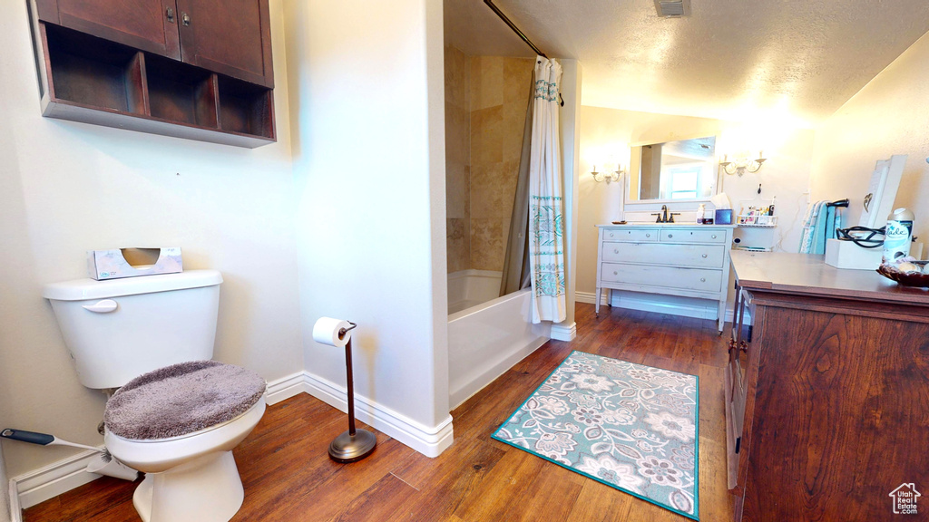 Full bathroom with hardwood / wood-style flooring, toilet, shower / tub combo, a textured ceiling, and vanity