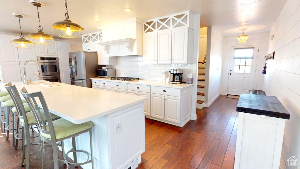 Kitchen featuring dark hardwood / wood-style flooring, stainless steel appliances, white cabinetry, backsplash, and a kitchen bar