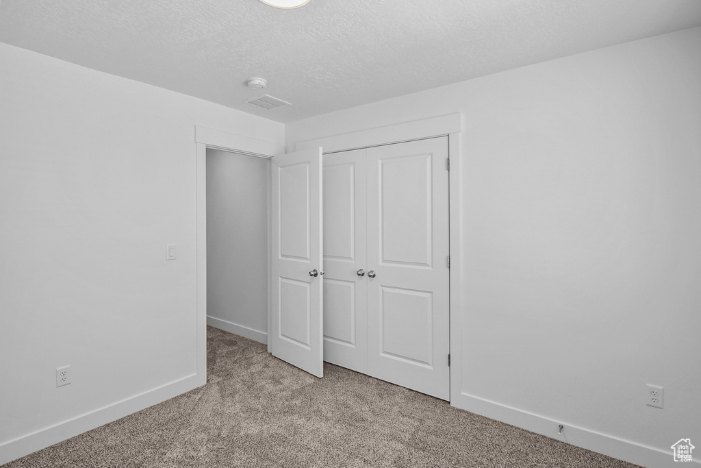 Unfurnished bedroom featuring a closet, light carpet, and a textured ceiling