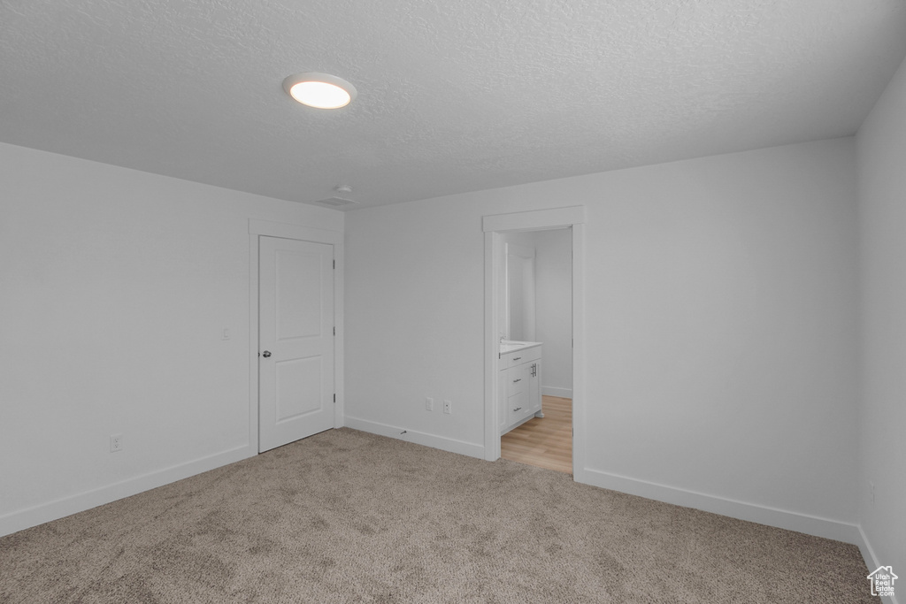 Unfurnished bedroom featuring light colored carpet, ensuite bathroom, and a textured ceiling