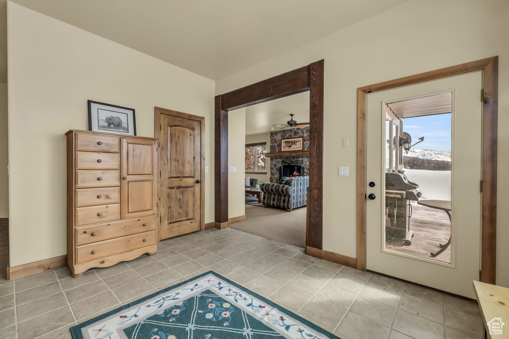 Doorway to outside featuring light tile flooring, ceiling fan, and a fireplace