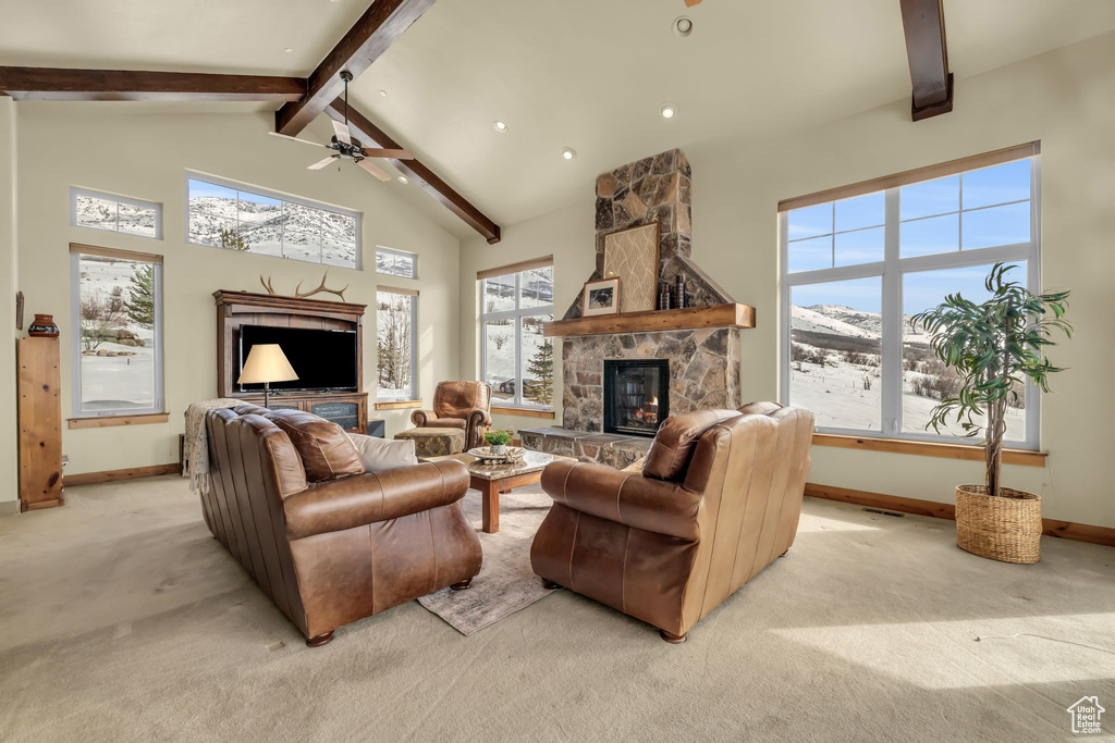Living room featuring high vaulted ceiling, a stone fireplace, light carpet, beam ceiling, and ceiling fan