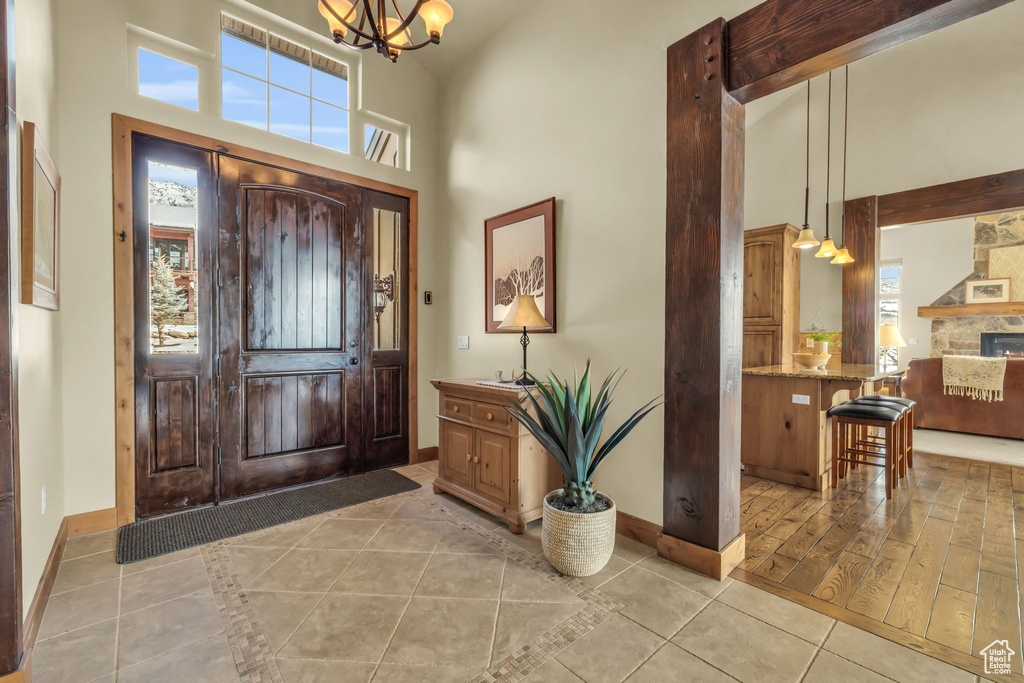 Tiled foyer featuring a high ceiling, a notable chandelier, and a stone fireplace