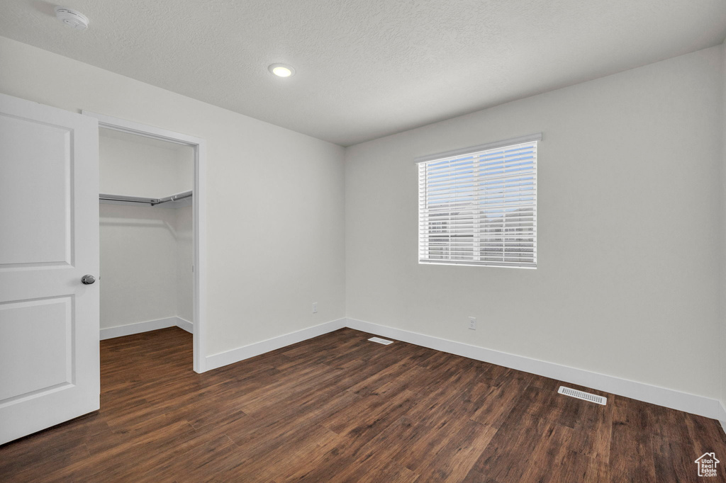 Unfurnished bedroom featuring a walk in closet, dark hardwood / wood-style flooring, and a closet