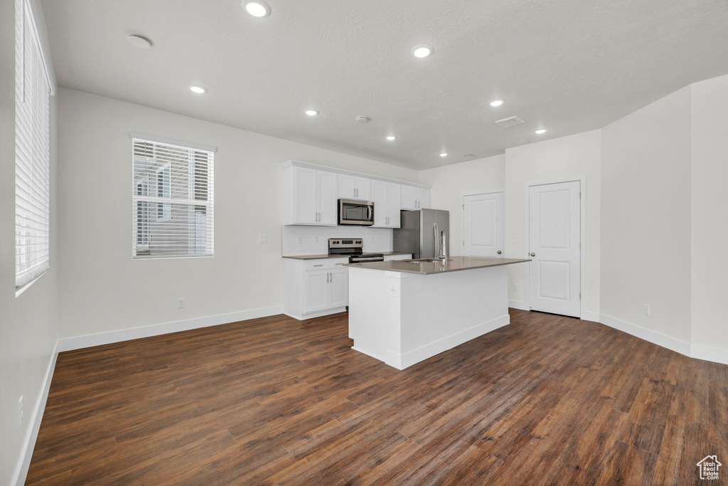 Kitchen featuring white cabinets, dark hardwood / wood-style floors, an island with sink, stainless steel appliances, and a healthy amount of sunlight