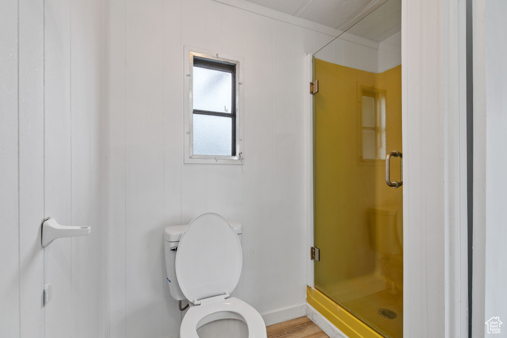 Bathroom with toilet, an enclosed shower, and wood-type flooring