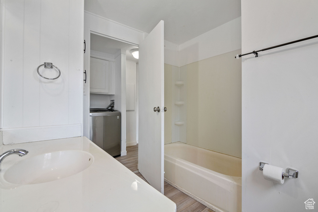 Bathroom featuring washtub / shower combination, washer / dryer, hardwood / wood-style flooring, and vanity