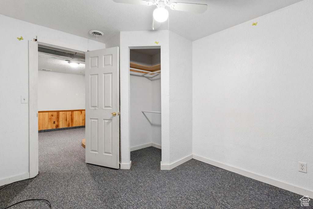Unfurnished bedroom featuring a closet, dark colored carpet, and ceiling fan