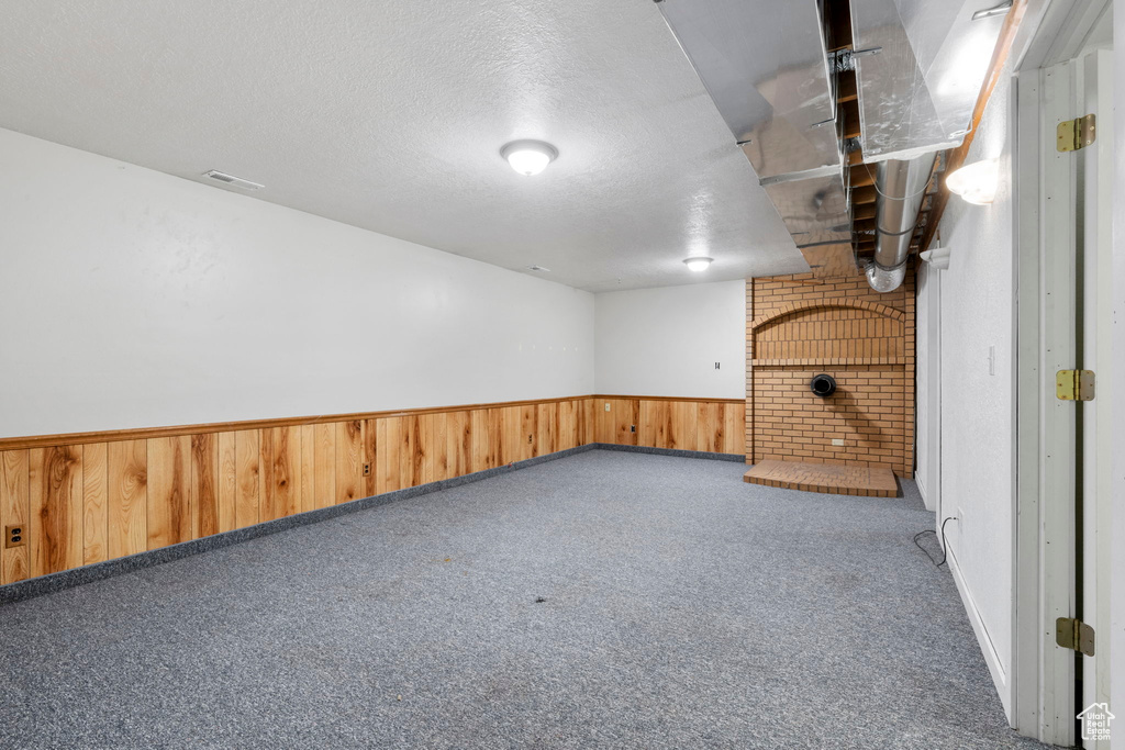 Basement with a textured ceiling, brick wall, and dark colored carpet