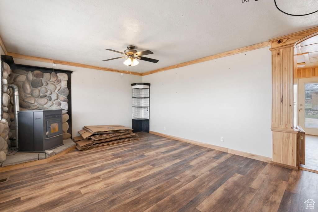 Unfurnished living room featuring dark hardwood / wood-style floors, ceiling fan, a wood stove, a textured ceiling, and crown molding
