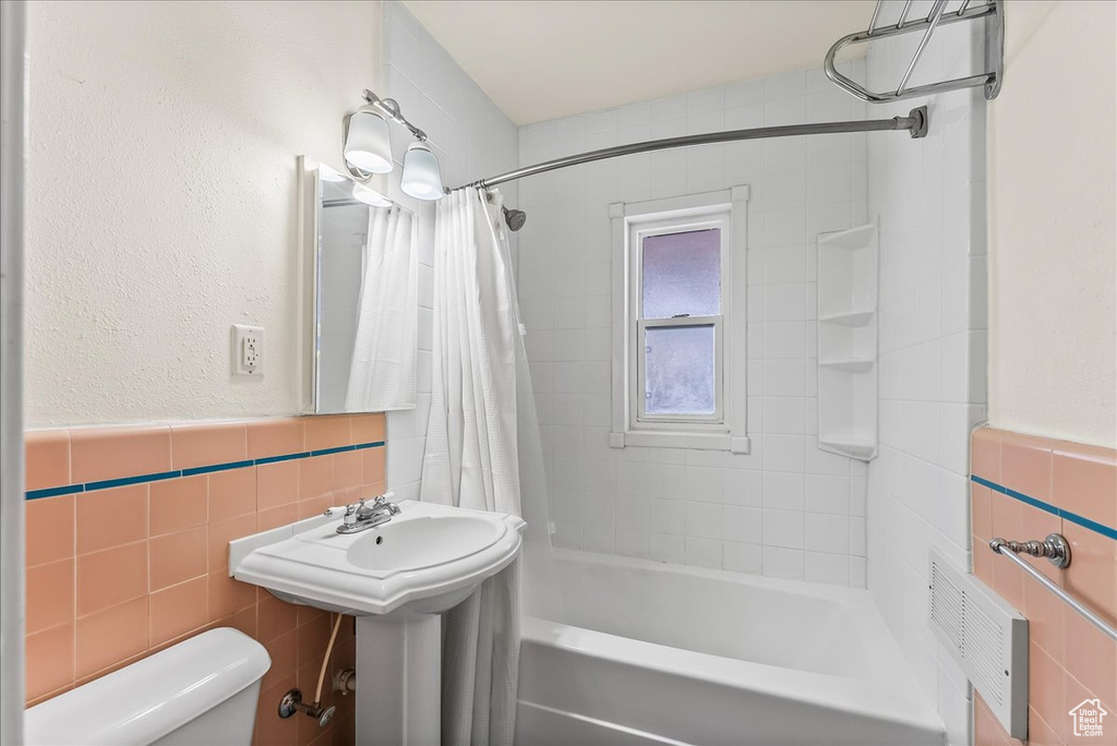 Bathroom featuring shower / bath combo with shower curtain, tile walls, tasteful backsplash, and toilet