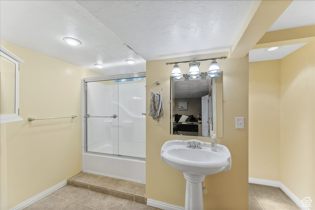 Bathroom with tile floors, bath / shower combo with glass door, and a textured ceiling